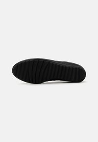 Suola di sneaker nera con scanalature testurizzate per la trazione. Presenta una forma curva e liscia ed è realizzata in materiale gommoso durevole.