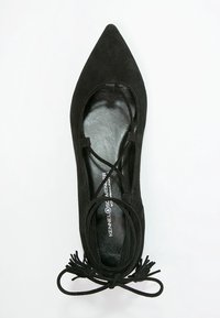 Zapato plano de ante negro con punta afilada, que presenta tiras entrecruzadas y un lazo decorativo en la parte delantera sobre una plantilla negra suave.