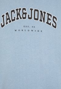 Svijetloplavi majica od mekog materijala s crnim zakrivljenim natpisom: "JACK&JONES EST. 90 WORLDWIDE." Glatka tekstura.