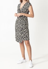 Czarna kopertowa sukienka w kwiaty z krótkimi rękawami, ozdobiona małymi białymi i żółtymi kwiatami. Miękki materiał, długość do połowy uda, zestawiona z białymi trampkami.