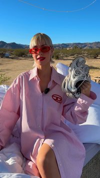 Camisa de botões às riscas vermelhas e brancas com um logótipo, combinada com sapatilhas de corrida prateadas e pretas, num cenário de deserto.