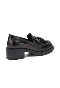 Mocasines de cuero negro con punta redondeada, con un acento de borlas y un tacón bajo de bloque. Textura suave con detalles de costura visibles.