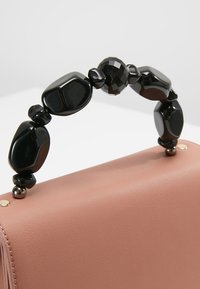 Sac à main en cuir rose avec une poignée composée de grosses perles noires polies et de petits connecteurs métalliques.