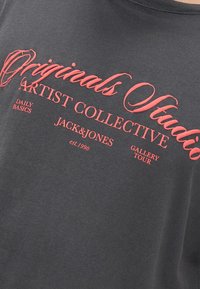 Melnas kokvilnas T-krekls ar īsām piedurknēm, ar sarkanu tekstu, kas lasāms "Originals Studio Artist Collective" un "Jack & Jones".