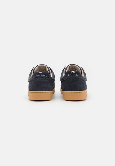 Et par navy suede sneakers med tan gummisåler sett fra baksiden, som viser "PS Paul Smith"-merket på hælflikene.