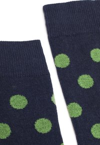 Chaussettes tricotées bleu marine avec de grands pois verts et des bords côtelés, présentées à plat sur un fond blanc.