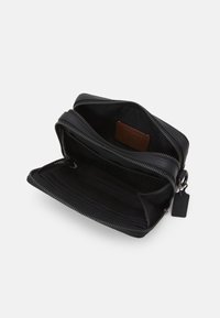 Portafoglio in pelle nera con zip argentata, dotato di due scomparti, uno dei quali con dettagli in rete, e un'etichetta in pelle marrone all'interno.