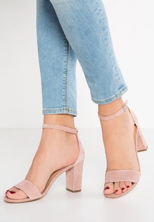 Różowe sandały na wysokim obcasie z odkrytymi palcami, wykonane z zamszu, z szerokim obcasem i paskiem na kostce. Paski są gładkie z subtelną fakturą.