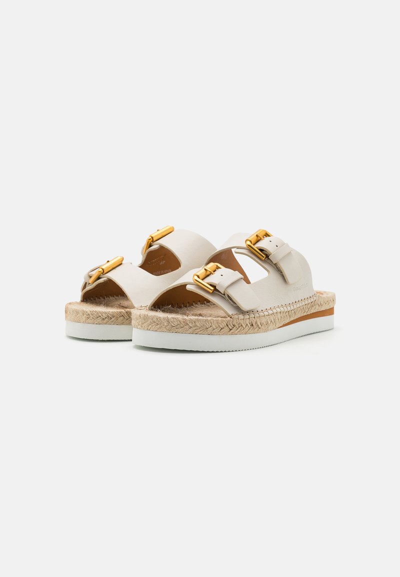 Beige Sandalen mit zwei breiten Riemen, goldenen Metall-schnallen und einer gewebten Espadrille-Sohle. Strukturierte Oberfläche mit einer weißen Gummisohle.