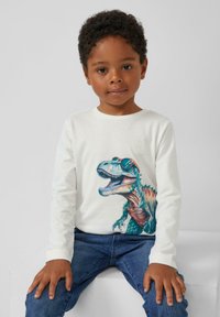 Weißes Langarmhemd mit einem bunten Dinosaurier-Motiv, der Sonnenbrille trägt. Das Kind trägt blaue Jeans. Schlichter Hintergrund.