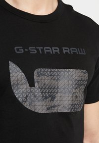 Camiseta de algodón negra con un gran logo gris texturizado con un patrón geométrico y el texto "G-Star RAW" en una fuente moderna y audaz.