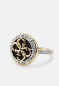 Ring i guldton med en svart cirkulär mittdel med präglad text, omgiven av klara ädelstenar längs bandet för extra detalj.