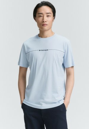 Lyseblå bomulds T-shirts med korte ærmer, udstyret med et marineblåt logo og en dekorativ stiklinje over brystet. Glat tekstur.