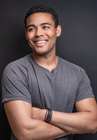 Gray short-sleeve t-shirt with a subtle texture, paired with a black woven bracelet, arms crossed against a dark background.