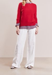 Maglione lavorato a maglia rosso su una camicia colletto a righe blu e bianche, abbinato a pantaloni larghi in lino bianchi e scarpe piatte metalliche.