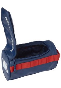 Mörkblå necessär med dragkedja och röd handtag; tillverkad av slitstarkt material, med en meshnäsa inuti och en iögonfallande vit logotyp på sidan.