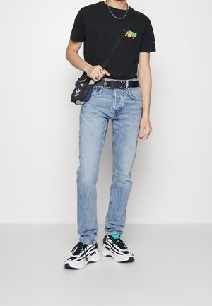 T-shirt noire avec impression colorée, jeans en denim bleu clair, ceinture noire et baskets multicolores. Comprend un sac à épaule noir camouflage.