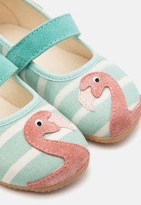 Šviesiai mėlyni ir balti dryžuoti drobiniai batai su rožiniu flamingo aplikacija, turintys Velcro dirželį ir tekstūruotą gumos padenkę.