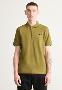 Camisa polo verde oliva hecha de un tejido texturizado, con cuello, mangas cortas y un pequeño logotipo negro en el pecho.