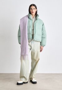 Giacca a sacco verde menta, maglia bianca a maglia, pantaloni di denim chiaro e sciarpa lavanda. Scarpe bianche oversize, orli sfrangiati e vestibilità morbida.