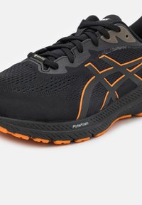 Crne atletske cipele napravljene od prozračnog mrežastog materijala, s narančastim detaljima, teksturiranom potplatom i natpisom "FlyteFoam" sa strane.