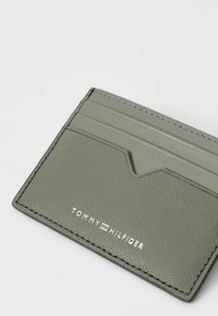 Portofel verde texturat cu cinci sloturi, margini cusute si un logo argintiu. Prezintă un design minimalist și un profil subțire.