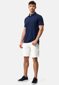 Marineblå polo med ensfarget design, laget av bomull, kortermet, med en subtil logo. Kombinert med hvite shorts og marineblå joggesko.