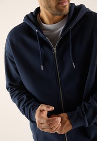 Felpa con cappuccio blu navy con zip, realizzata in tessuto morbido, dotata di cappuccio con coulisse, cerniera argentata e polsini a costine. Tessuto liscio.