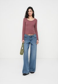 Μακρυμάνικο crop top με ριμπ ύφανση σε βυσσινί, ψηλόμεσο ανοιχτό μπλε παντελόνι με φαρδιά μπατζάκια και μικρή πράσινη τσάντα. Μαύρα παπούτσια με επίπεδη σόλα.