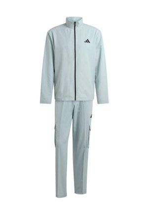 Jasnoszary dres sportowy wykonany z gładkiego materiału. Posiada wysoki kołnierz, zamek błyskawiczny oraz czarne akcenty logo na kurtce i spodniach.