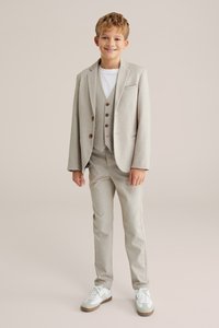 Šviesiai pilkas kostiumas su švarku, liemene ir kelnių. Po juo balta marškinėlė. Batai su baltais ir šviesiai pilkais akcentais. Lygus audinys.