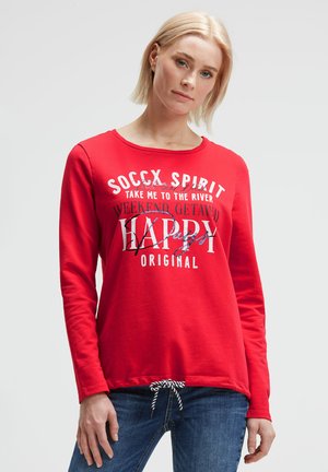 Rotes Langarmoberteil mit Rundhalsausschnitt. Mit bedrucktem Text in Weiß und Schwarz sowie einem Kordelzugsaum mit gestreiftem Muster.