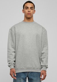 Sudadera gris con cuello redondo y puños acanalados, que presenta un ajuste relajado y un tejido suave y texturizado, combinada con vaqueros azules.