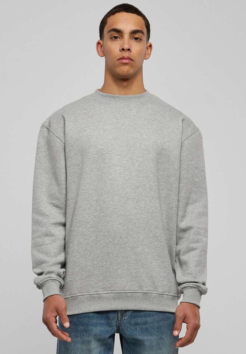 Sudadera gris con cuello redondo y puños acanalados, que presenta un ajuste relajado y un tejido suave y texturizado, combinada con vaqueros azules.