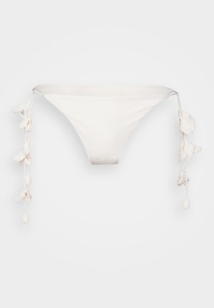 Parte inferior de bikini blanca con forma triangular, que presenta una tela texturizada y borlas decorativas en cada lado.