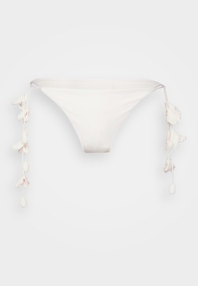 Hvid bikini bund med en trekantet form, der har tekstureret stof og dekorative frynser i hver side.