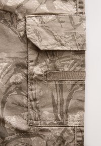 Tessuto mimetico beige con tasca laterale con patta, cuciture rinforzate e sezione con asola testurizzata per l'aggancio.