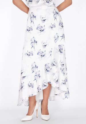 Biała asymetryczna spódnica z fioletowym kwiatowym wzorem, noszona z białymi szpilkami, odsłaniająca dolne części nóg i część tułowia.