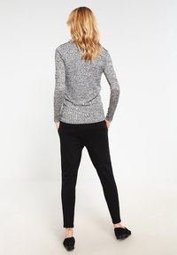 Szary, teksturowany longsleeve z dopasowanym krojem, zestawiony z czarnymi spodniami tapered i czarnymi butami. Widok z tyłu, minimalistyczny styl.
