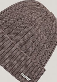 Brązowa dzianinowa czapka z tkaniny, z prążkowaną fakturą, z podwiniętym mankietem i małą metalową metką z logo po boku.