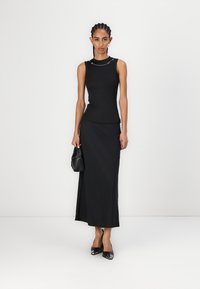 Haut sans manches noir au design ajusté, associé à une jupe maxi fluide noire. Des talons hauts noirs et un petit sac à main noir complètent le look.
