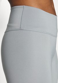 Jasnoszare legginsy z wysokim stanem wykonane z gładkiego, elastycznego materiału. Posiadają wzmocnione szwy oraz elegancki, dopasowany krój.