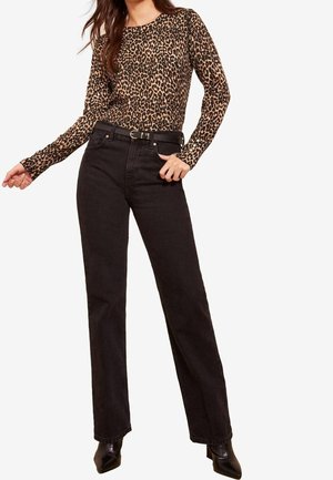 Femme portant un haut à manches longues imprimé léopard, un jean noir taille haute avec une ceinture noire, et des bottines noires pointues.