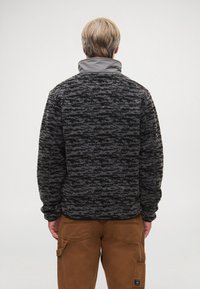 Chlpatý čierny a sivý fleece pulóver s vysokým golierom, textúrovaným vzorom a elastickými manžetami, skombinovaný s hnedými cargo nohavicami.