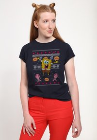 Camiseta de algodón azul marino con un gráfico colorido de SpongeBob acompañado de medusas rosas y acentos de patrón, combinada con pantalones ajustados rojos.