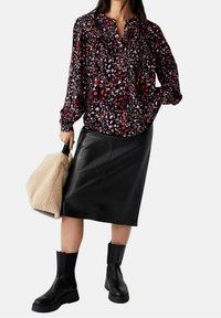Blusa nera a stampa floreale con maniche lunghe, abbinata a una gonna in pelle nera aderente e stivali neri alla caviglia. Borsa beige strutturata.