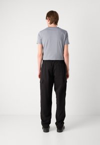 T-shirt clair gris à manches courtes associé à un pantalon cargo noir avec poches latérales et taille élastique, vu de l'arrière.