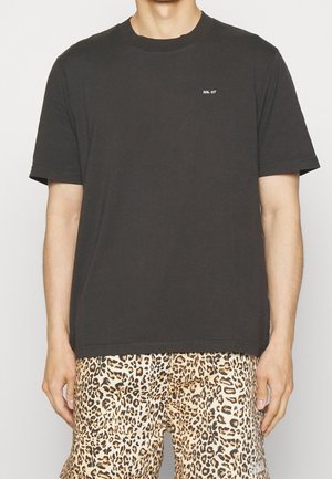Man wearing plain dark gray t-shirt with small white "NN. 07" logo and leopard print shorts with hands relaxed at sides.
