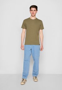Oliven grønn kortermet t-skjorte kombinert med lyseblå stripete denimbukser og beige sneakers. Outfitten har en avslappet passform.