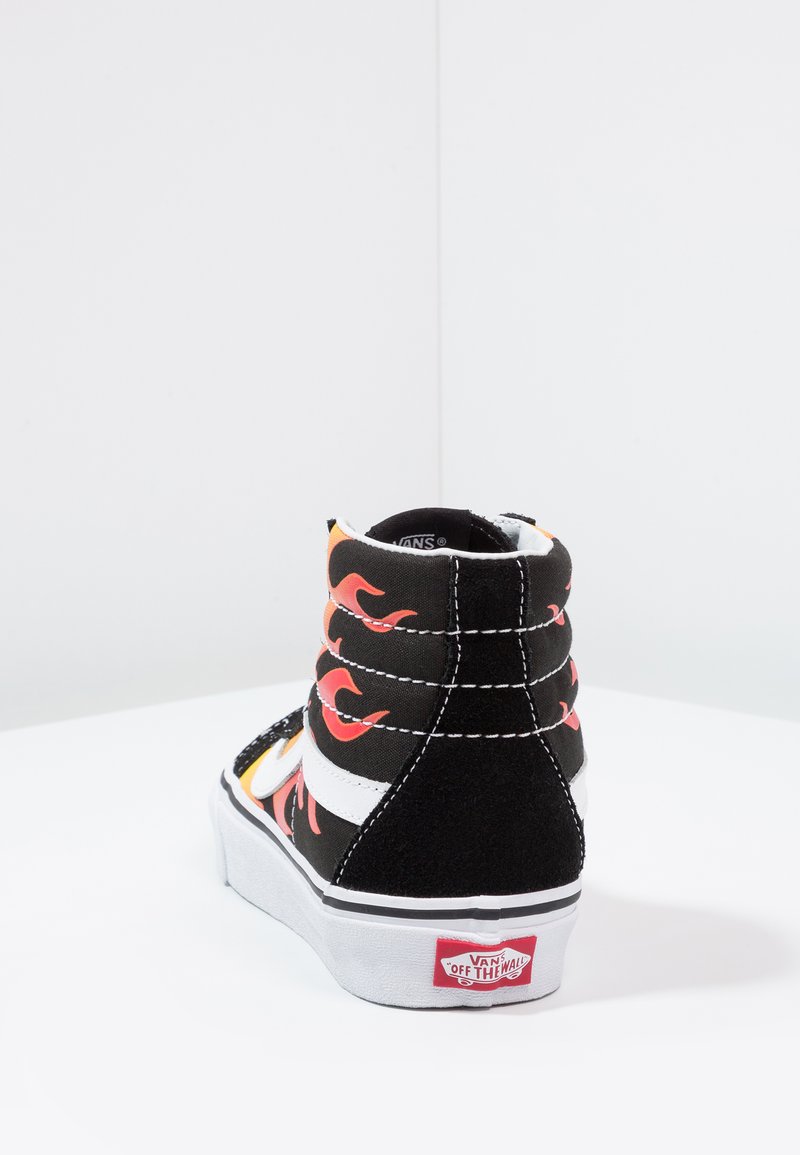 Zwarte high-top sneaker met rode vlampatronen, witte strepen, zwarte suède accenten en een rubberen zool met het Vans-logo op de hiel.
